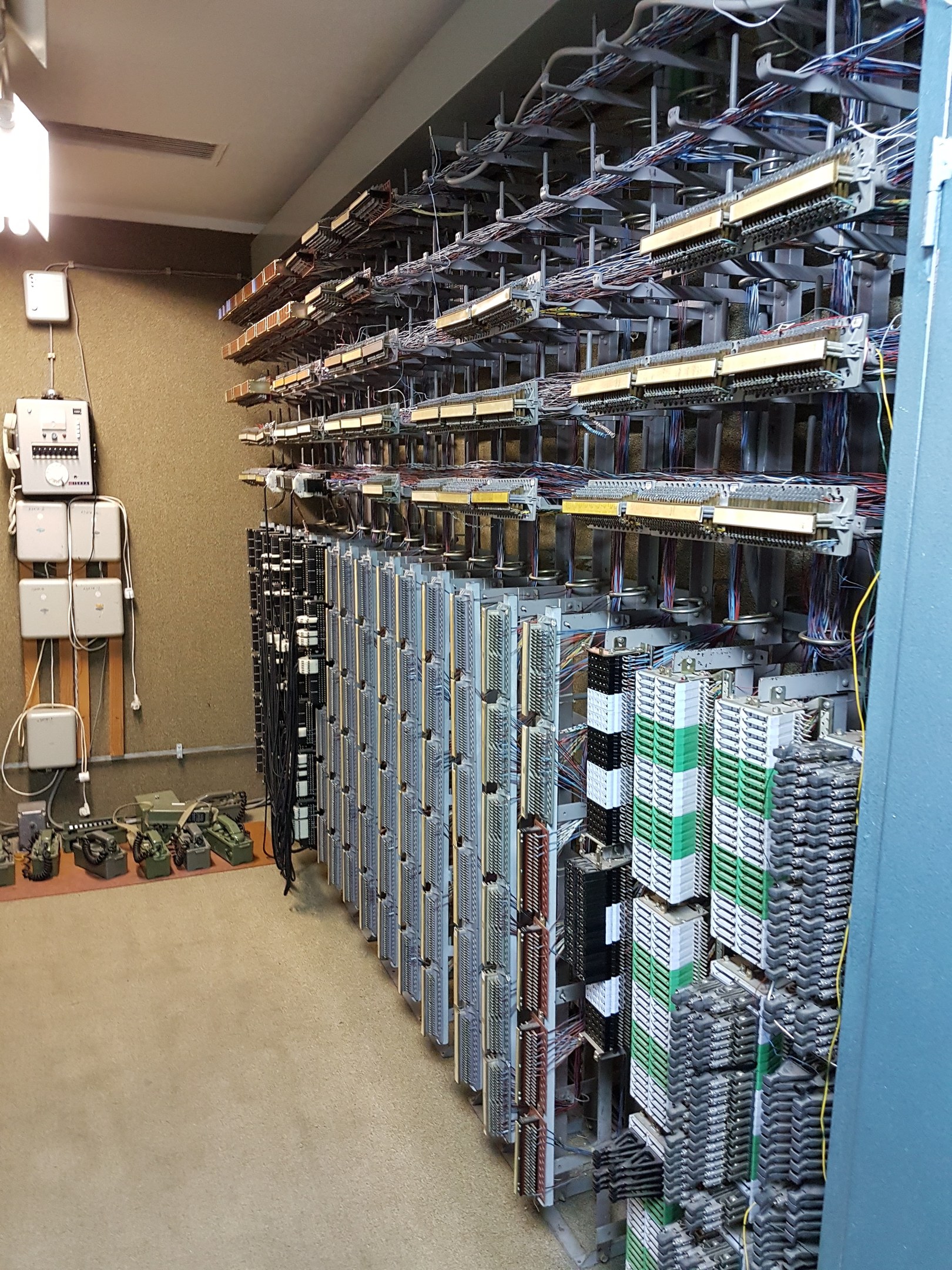 Großer Raum voller numerous Wires und elektronische Geräte auf dem Boden, einschließlich Server und Kabel, was auf ein Rechenzentrum mit einer sichtbaren Wand auf der linken Seite hinweist.