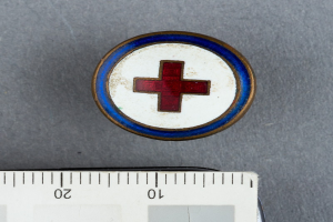 Ein rotes Kreuz auf einem weißen Hintergrund mit einem Lineal daneben, das ein medizinisches Abzeichen darstellt, mittig mit einer Waage unten.