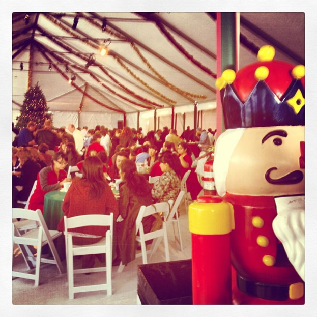 Eine Gruppe von Menschen, die Weihnachten in einer Hütte feiern, mit einem geschmückten Baum, weißen Stühlen, einem roten Spielzeug-Sicherheitsmann und einer schwarzen Krone.