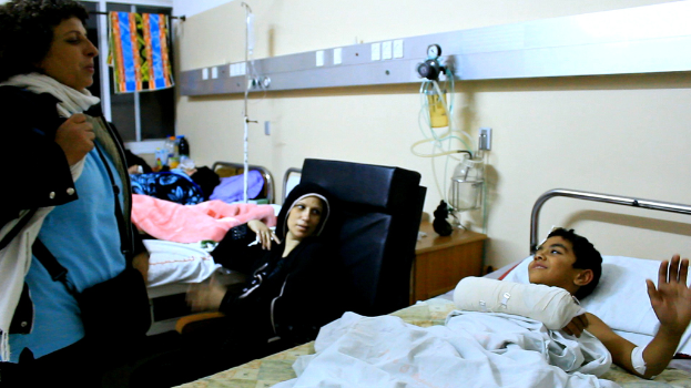 Ein Blick in eine Krankenhausstation mit besetzten Betten, Infusionsflaschen auf StÃ¤nden zwischen den Betten und einer Frau mit einer Tasche in der NÃ¤he eines Patienten.