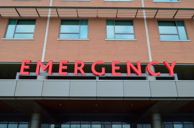 Ein Gebäude mit Glasfenstern, Säulen und einem sichtbaren roten Notfallzeichen, das es als Notaufnahme ausweist.