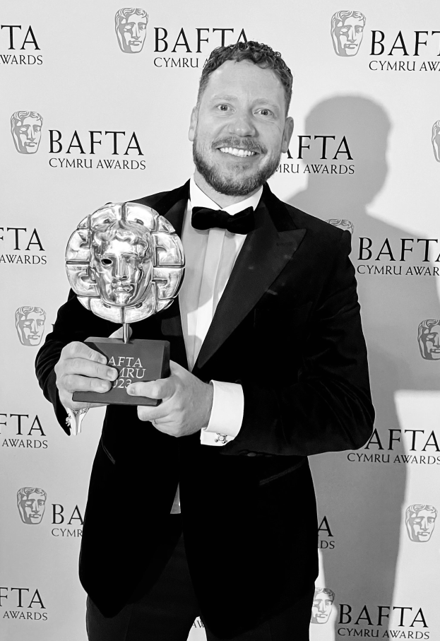 Ein Mann im Smoking, der eine BAFTA-Auszeichnung hält, vor einer Tafel mit der Aufschrift "BAFTA Awards 2018."