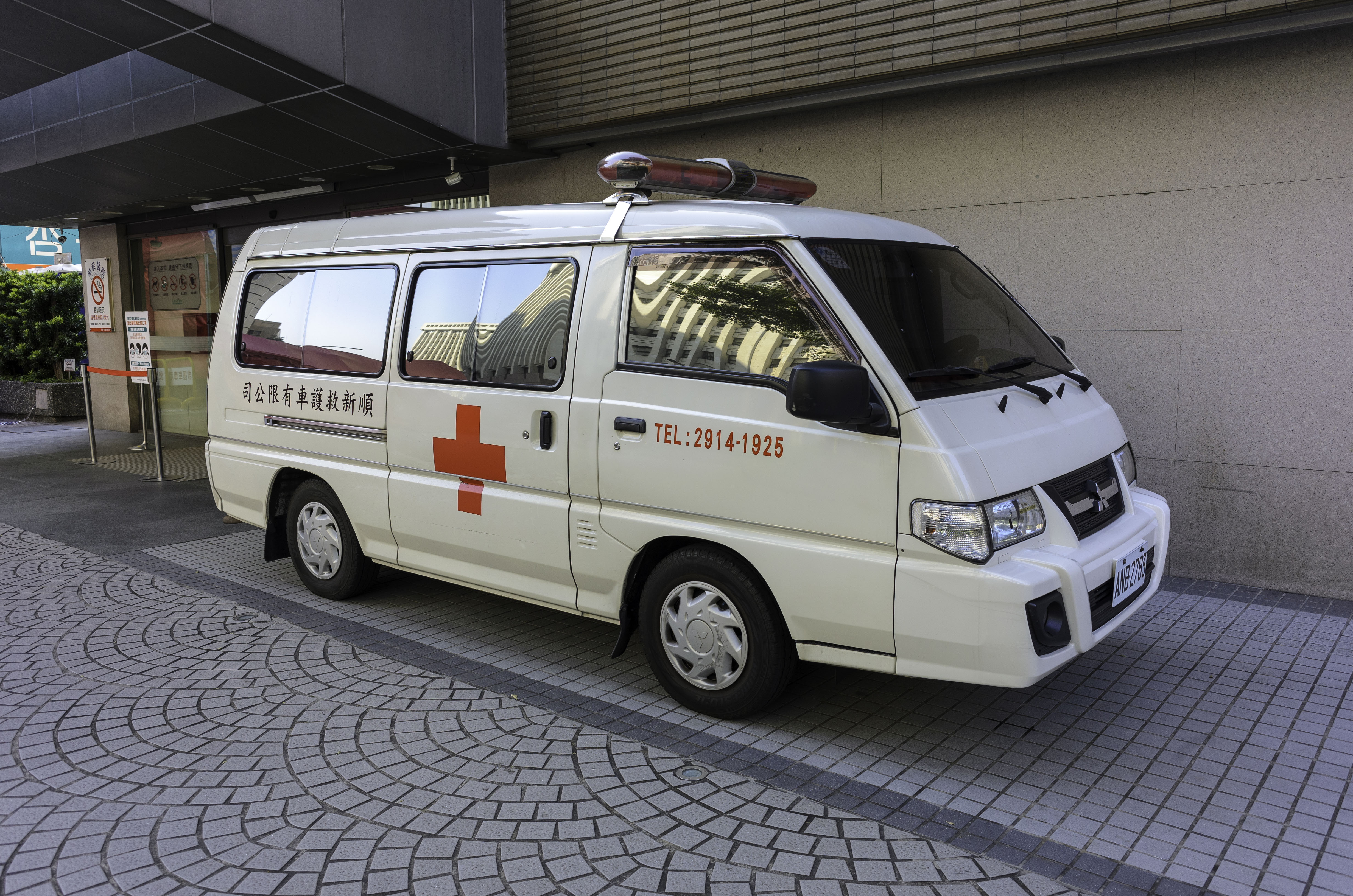 Ein Rettungswagen steht vor einem Gebäude mit einer Tafel, umgeben von Bäumen und Pflanzen.