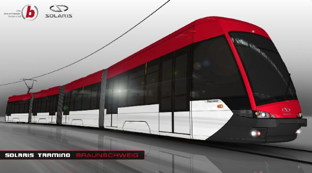 Eine rote und weiße Straßenbahn mit der Aufschrift "Solaris Tramino Braunschweig" auf einem Gleis mit Strommasten und -leitungen im Hintergrund.
