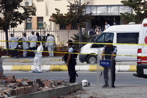 Eine Gruppe von Polizisten steht vor einem Gebäude mit Fenstern, umgeben von Fahrzeugen, einem Zaun, Bäumen, Pflanzen und Steinen, mit einem Helm im Vordergrund, wahrscheinlich nach einer Bombenexplosion in Mexiko-Stadt.