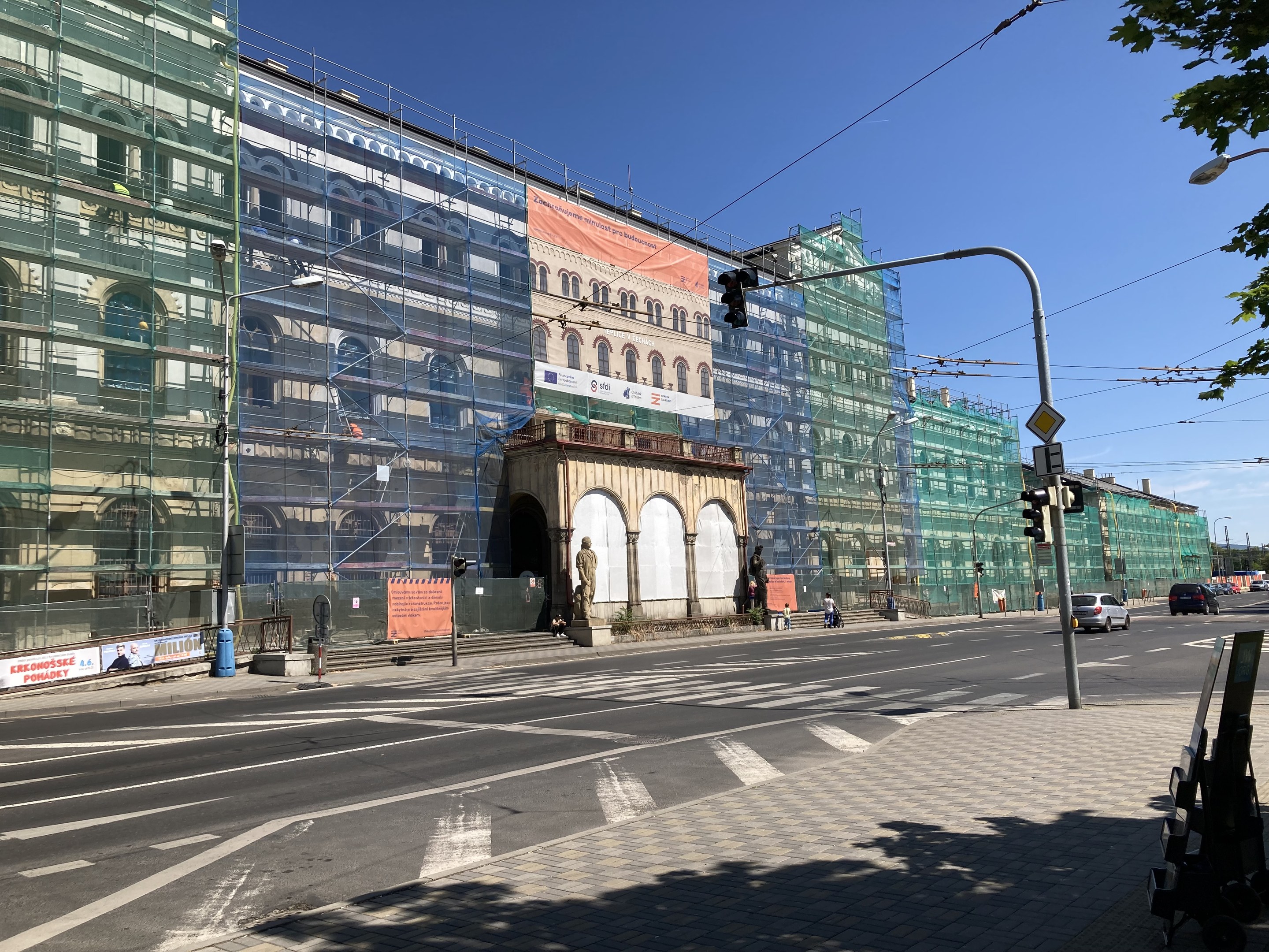 Großer mehrgeschossiger Bau unter construction in Berlin mit zahlreichen Fenstern, umgeben von Straßeninfrastruktur, Fahrzeugen, Fußgängern und Bäumen unter einem bewölkten Himmel.