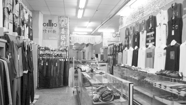 Eine Ausstellung von Kleidung, Gürteln und Schuhen mit einer Uhr an der Wand, hängendem Stoff, Lichtern und einem Banner mit Text auf der linken Seite.