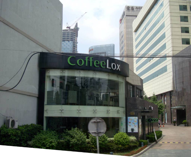 Ein Geschäftsgebäude mit einigen Pflanzen davor, umgeben von vielen hohen Gebäuden und einigen Drähten.