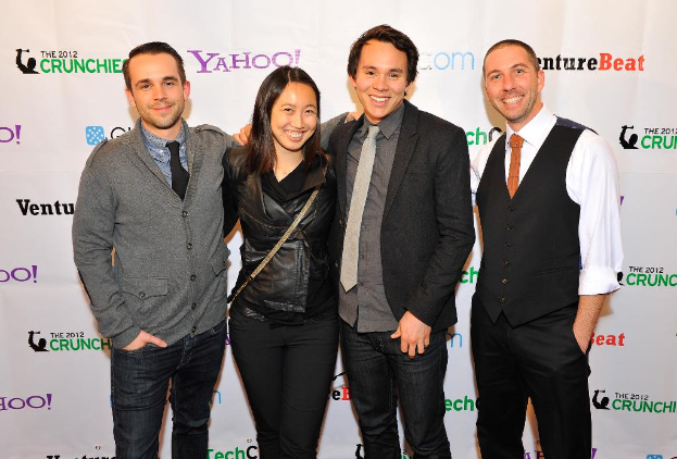 Eine Gruppe strahlender Menschen, die vor der Kamera posieren, mit einem Sponsorenbanner im Hintergrund.