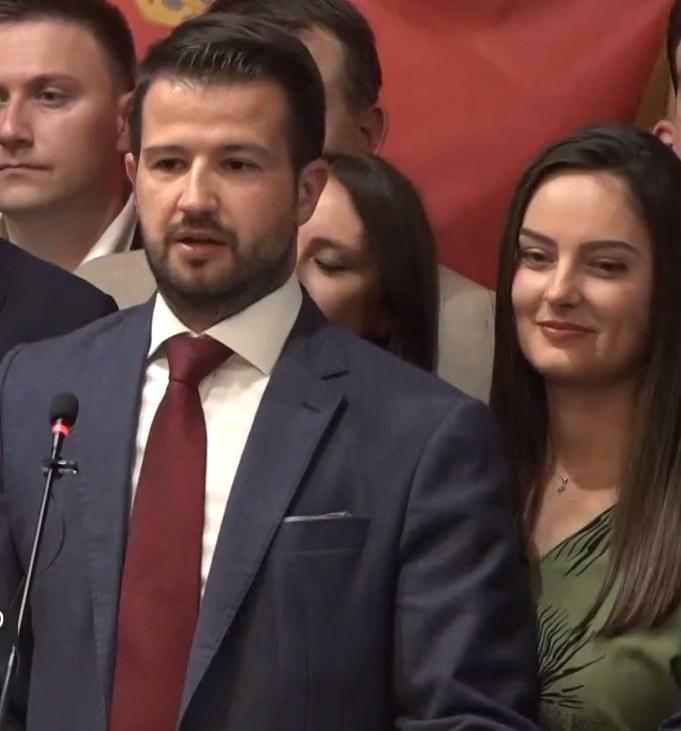 Ein Mann im Anzug spricht an einem Rednerpult mit einem Mikrofon zu einer Menge hinter einem Banner, wahrscheinlich über ein Verbot von Social Media durch die Regierung.