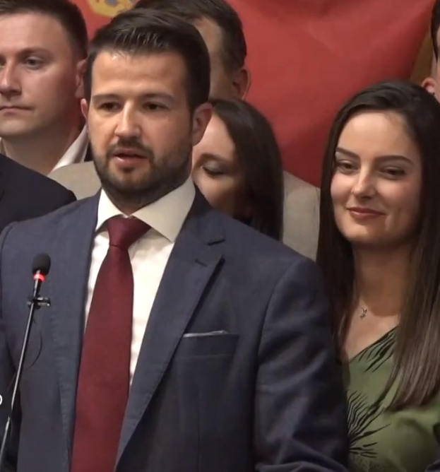 Ein Mann im Anzug spricht an einem Rednerpult mit einem Mikrofon zu einer Menge hinter einem Banner, wahrscheinlich über ein Verbot von Social Media durch die Regierung.