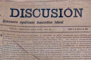 Ein gelblich, leicht zerknittertes Zeitungsblatt mit der Aufschrift "Diskussion" in schwarzer Tinte, das die Überschrift "Semanario Repúblicano Democrático Federal" trägt.
