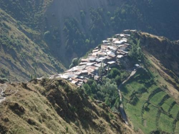 Kleines Dorf mit Häusern, die zwischen saftigen grünen Hügeln und Bäumen in einer Berglandschaft liegen.