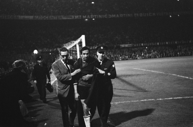 Schwarzes Bild von Fußballspielern, die auf einem Feld mit Torpfosten und beleuchteter Stadionkulisse feiern.