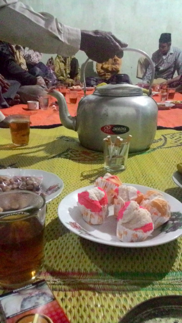 Ein Raum mit wenigen Menschen und einem Tisch mit Tellern, Gläsern und Lebensmitteln.