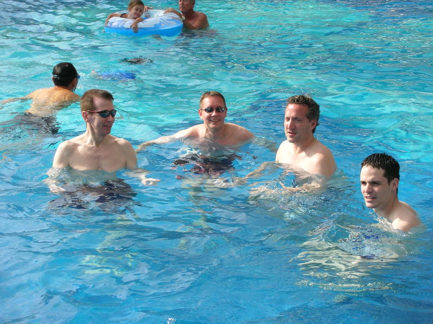Mehrere Männer schwimmen im Wasser, während ein Mädchen mit einem Ballon schwimmt, den jemand anderes hält.