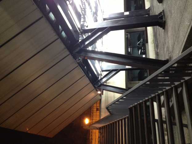 Treppen mit Geländern in der rechten unteren Ecke, Säulen auf der rechten Seite des Bodens, Autos in Gebäuden hinter den Säulen, Lampen und Decke auf der linken Seite.