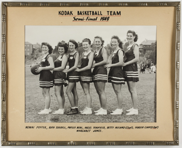 Schwarzes und weißes Foto einer Gruppe von Frauen, die lächeln und einen Basketball halten, mit der Aufschrift "Kodak Basketball Team Semi-Final 1949" oben und unten.