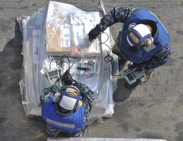 Zwei Männer in blauen Uniformen und Helmen arbeiten an einem großen Drohnen, hölden verschiedene Gegenstände, während eine Plastikhölle auf dem Boden liegt.