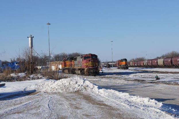 Eine Lokomotive vorne mit einem Eisenbahnwagen auf der rechten Seite auf den Schienen geparkt, Schnee auf dem Boden, trockene Bäume und ein Strommast im Hintergrund.
