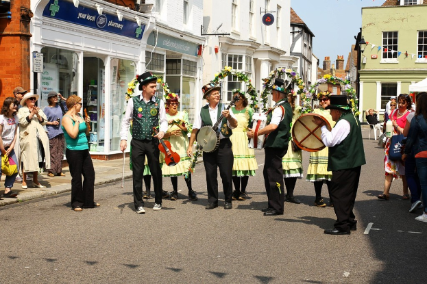 Eine Gruppe von Musikern spielt Instrumente auf der Straße, umgeben von einer kleinen Menge und Geschäften mit Schildern im Hintergrund.