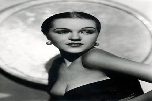 Ein Schwarz-Weiß-Foto einer Frau in einem langen, hochgeschlossenen Kleid mit 1940er-Jahre-Stil und Make-up, die selbstbewusst in die Kamera schaut, mit einem unscharfen Hintergrund und Text unten.