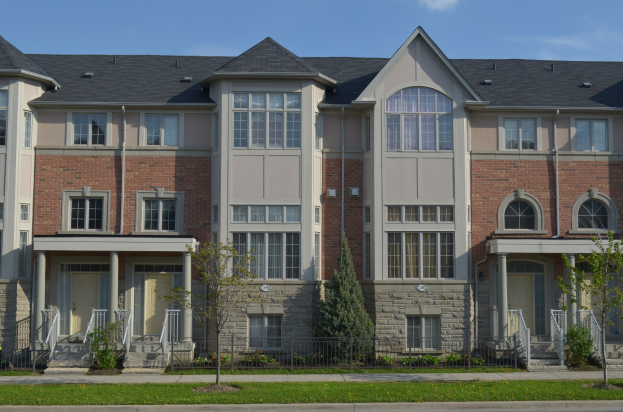Eine Reihe von Stadthäusern in einem Wohnviertel, mit Fenstern, Türen, Säulen, Geländern, Treppen und Grün, mit einer Straße im Vordergrund und dem Himmel im Hintergrund.