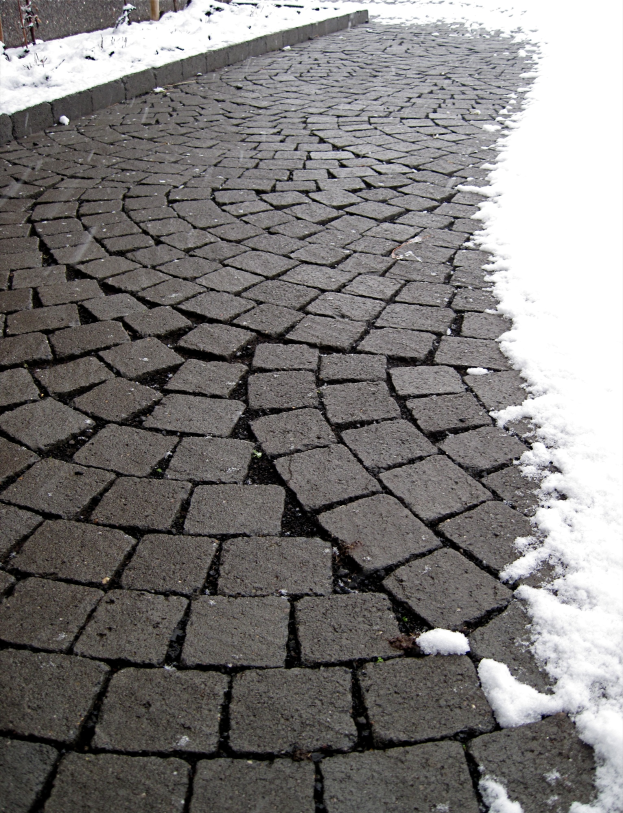 Eine Kopfsteinpflasterstra{ße mit einer leichten Schneeschicht, ein Zaun ist im Hintergrund zu sehen.