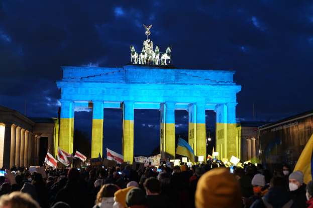 Eine Menschenmenge steht vor dem Brandenburger Tor in Berlin, Deutschland, mit Fahnen und Schildern, auf denen ein Banner auf der rechten Seite zu sehen ist.