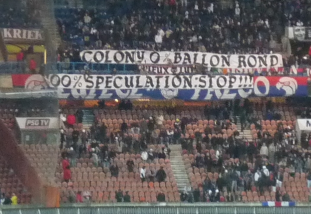Eine große Menschenmenge in einem Stadion mit Bannern und Stühlen im Vordergrund, einem Zaun unten und einer Treppe auf der linken Seite.