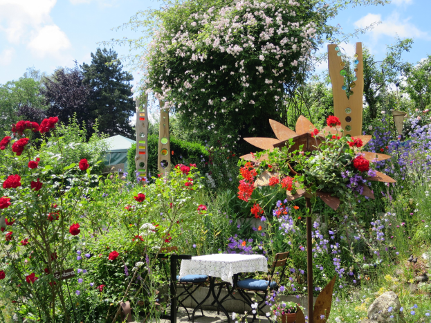 Ein Garten auf der Chelsea Flower Show mit farbenfrohen Blumen und Pflanzen, einem Tisch mit einer Decke in der Mitte, umgeben von Bäumen unter einem bewölkten Himmel.