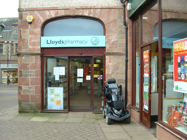 Eine Apotheke mit einem vor dem Eingang geparkten Auto und einem Gebäude in der linken Ecke.