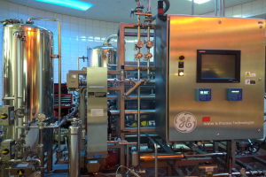 Eine große Maschine in einer Wasseraufbereitungsanlage, umgeben von verschiedenen Geräten, mit einer Wand im Hintergrund und einer Decke mit Leuchten oben.