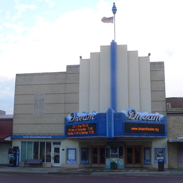 Außenansicht des Dream Theaters in St. Louis, Missouri, mit Glastüren und -fenstern, einem Namen Schild, einer Bank, einem Müllbehälter und einer Flagge auf dem Dach unter einem bewölkten Himmel.