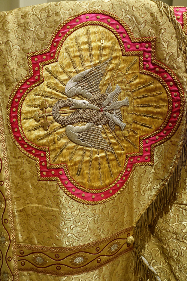 Nahaufnahme eines Priestergewandes mit aufwendiger Gold- und Roterie und luxuriösem Design vor einer Wand im Hintergrund.
