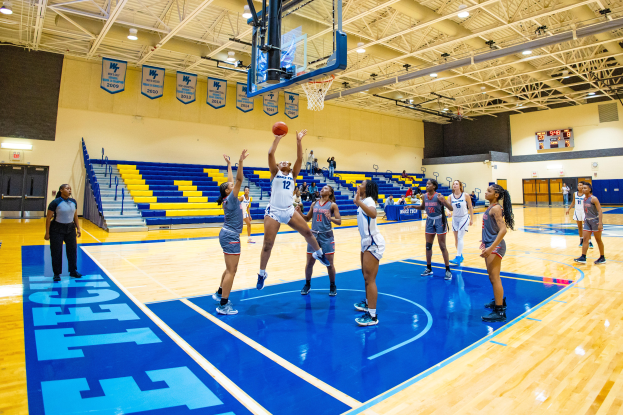 Eine Gruppe von Frauen, die Basketball in einer Turnhalle mit einem Scoreboard spielen, das ihren NCAA-Turniersieg anzeigt.