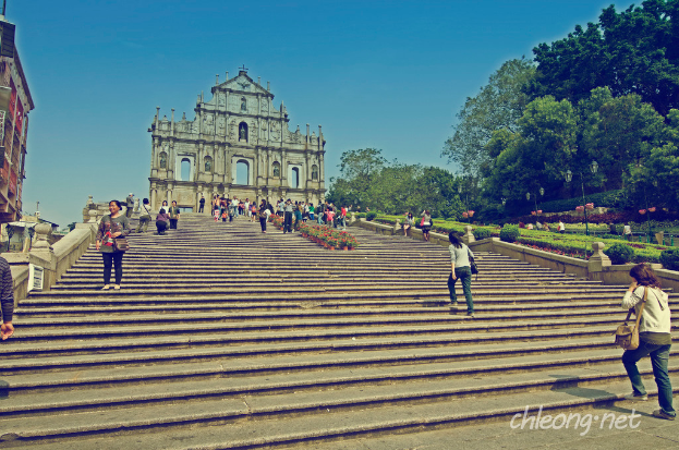 Ein Denkmal mit vielen Stufen davor, umgeben von zahlreichen Menschen und Bäumen auf der rechten Seite.