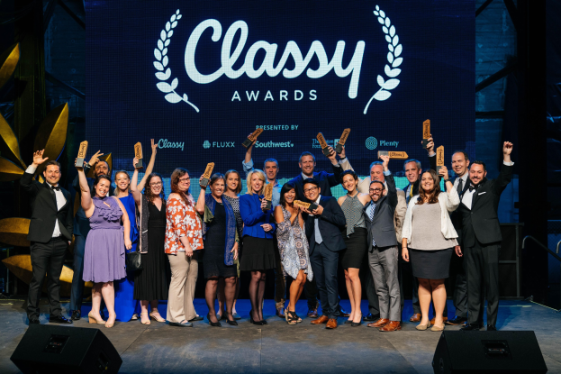 Gruppe von Menschen auf einer Bühne, die Auszeichnungen halten, mit Rednern darunter und einem Bildschirm im Hintergrund mit "Classy Awards 2019"