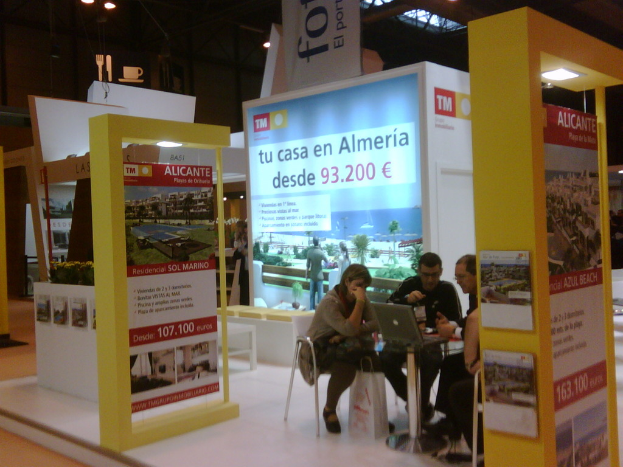 Eine Gruppe von Menschen sitzt an einem Tisch und schaut auf einen Laptop, mit mehreren Flyern mit verschiedenen Werbeanzeigen daneben.