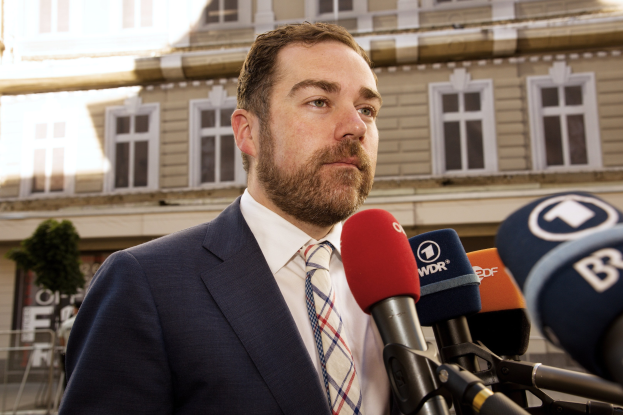 Ein Mann im Anzug spricht zu Reportern vor einem Gebäude, wahrscheinlich im Zusammenhang mit einer dreijährigen Haftstrafe.