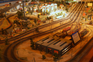 Eine Modellbahnanlage in einem Museum mit Gebäuden, Bäumen, Schienen, Fahrzeugen, Masten, Lichtern, Plakaten und anderen Gegenständen, die eine belebte Stadtlandschaft schaffen.