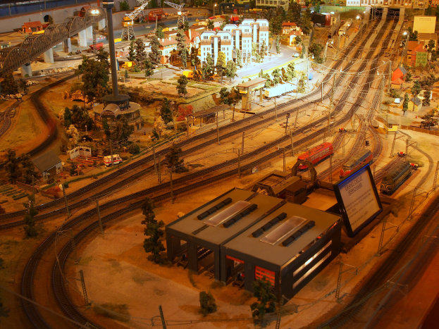 Eine Modellbahnanlage in einem Museum mit Gebäuden, Bäumen, Schienen, Fahrzeugen, Masten, Lichtern, Plakaten und anderen Gegenständen, die eine belebte Stadtlandschaft schaffen.