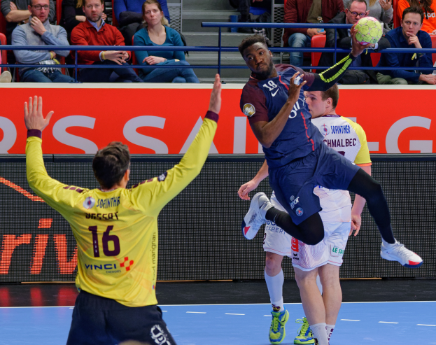 Eine Gruppe von Männern, die auf einem Feld Handball spielen, mit einem Ball in der Luft und Zuschauern im Hintergrund, und einem Schild mit der Aufschrift "Futsal-Weltmeisterschaft 2019 - Paris Saint-Germain vs Bordeaux".