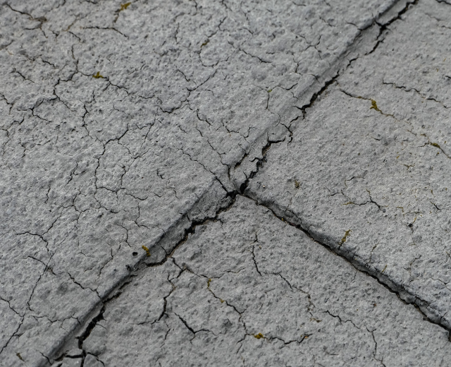 Nahaufnahme einer gebrochenen und verwitterten Straßenoberfläche mit tiefen, breiten Rissen.