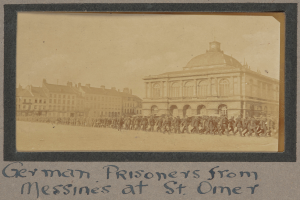 Eine Gruppe deutscher Gefangener aus Messines steht vor einem Gebäude mit einem klaren blauen Himmel im Hintergrund, mit Text unten im Bild.
