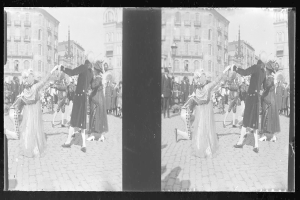 Ein Schwarz-Weiß-Foto einer Gruppe von Menschen, die auf der Straße tanzen, während eines Karnevals-Umzugs, mit Kostümen, umgeben von Gebäuden, Straßenlaternen und Straßenlaternen unter einem klaren Himmel.