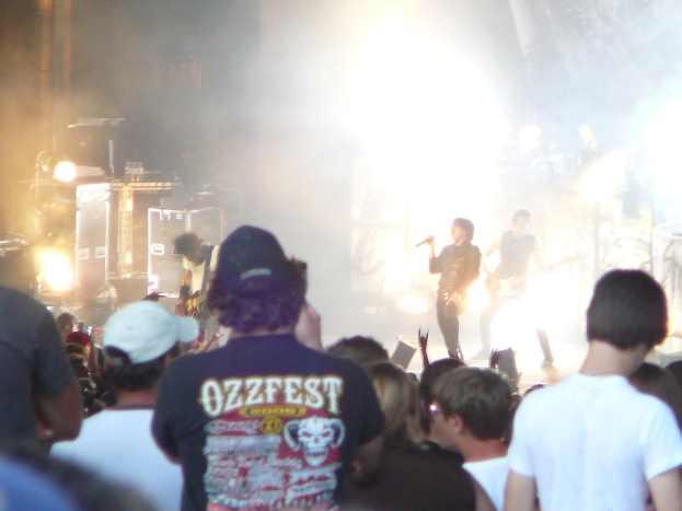 Eine Gruppe von Menschen in verschiedenen Kleidungsstücken, einige mit Mützen, in der Nähe von Musikinstrumenten wie einer Gitarre und einem Mikrofon, mit Bühnenscheinwerfern.