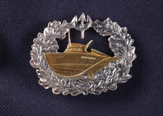 Ein gold-silbernes Abzeichen mit einem Boot, das die deutsche Marine repräsentiert, auf einem Tuch.