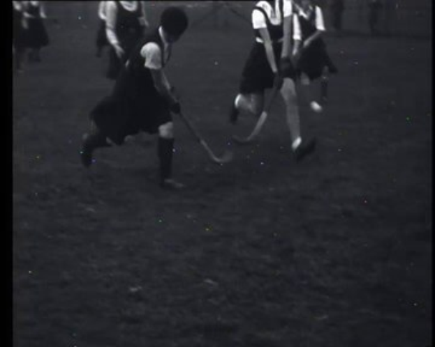 Schwarzes und weißes Foto einer Gruppe junger Mädchen, die auf einem Feld Hockey spielen und jeweils einen Hockeystock halten.