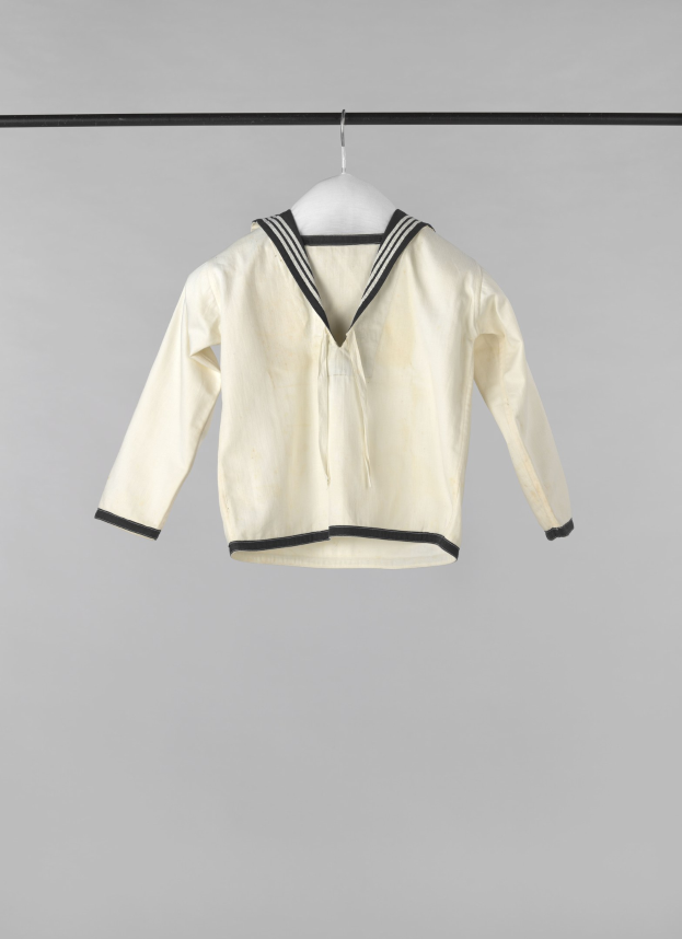 Weißer Matrosenstil-Jacke mit Kragen, langen Ärmeln und Knopfleiste, die an einer Wäscheleine an einem weißen Hintergrund hängt.